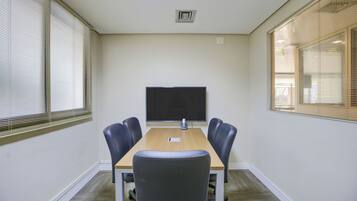 Une salle de conférence équipée d’une grande table, de quatre chaises, d’un téléviseur à écran plat et de fenêtres avec des stores.