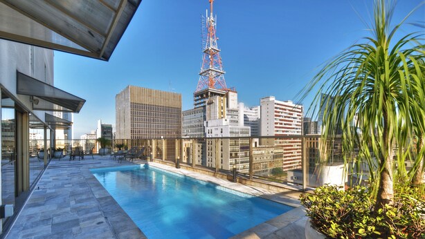 Piscina en la azotea con vista panorámica de la ciudad, incluyendo una alta torre de comunicaciones.