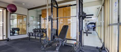 A modern gym with weightlifting equipment, a bench, and dumbbells.