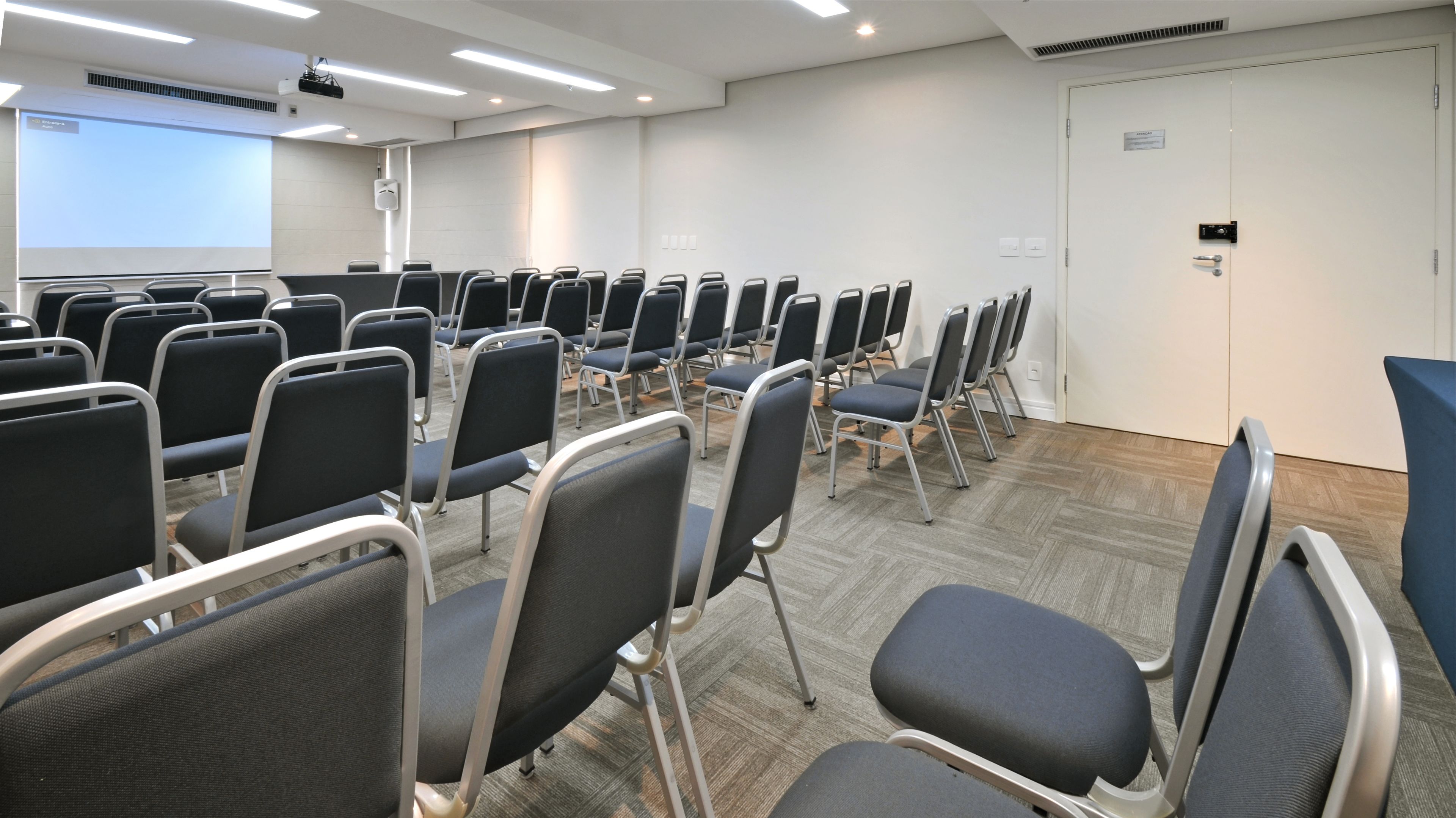 A conference room with rows of chairs, a projector screen, and a whiteboard.