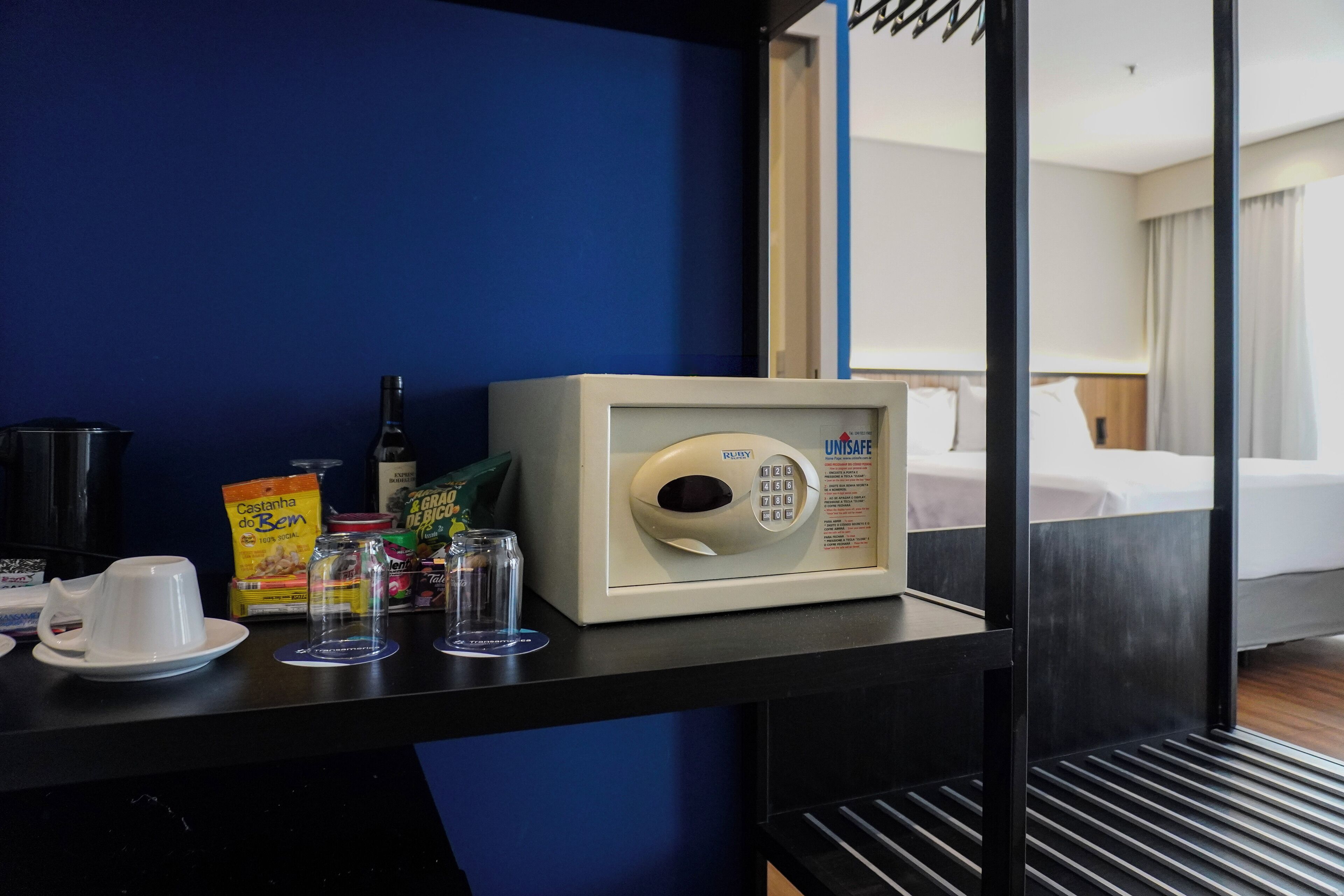A minibar with a microwave, a bottle, a glass, and some food items.