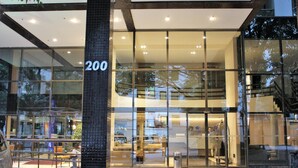 Una entrada de hotel moderna con fachada de vidrio, un interior visible con asientos y una escalera que conduce a un nivel superior.