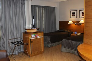 Camera d'albergo con due letti, una scrivania con televisione a schermo piatto, un minibar e un tavolino di legno con lampade.
