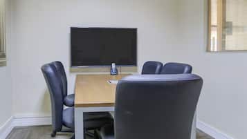 A conference room with a wooden table, four black office chairs, a flat-screen TV, and a ceiling vent.