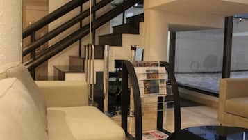 Sala de estar moderna com escada, mesa de centro de vidro e suporte para revistas.
