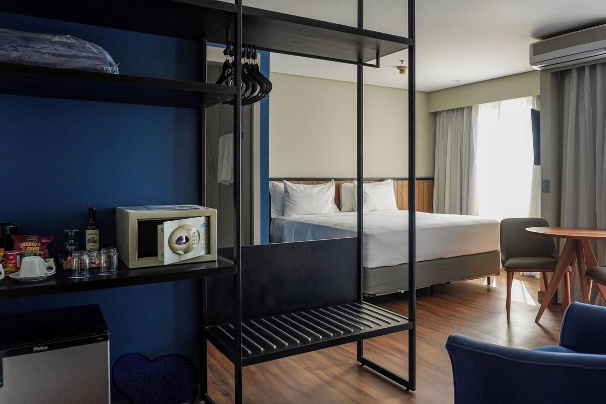 Una habitación de hotel con cama, escritorio con silla, mesita, sofá, armario y unidad de aire acondicionado.