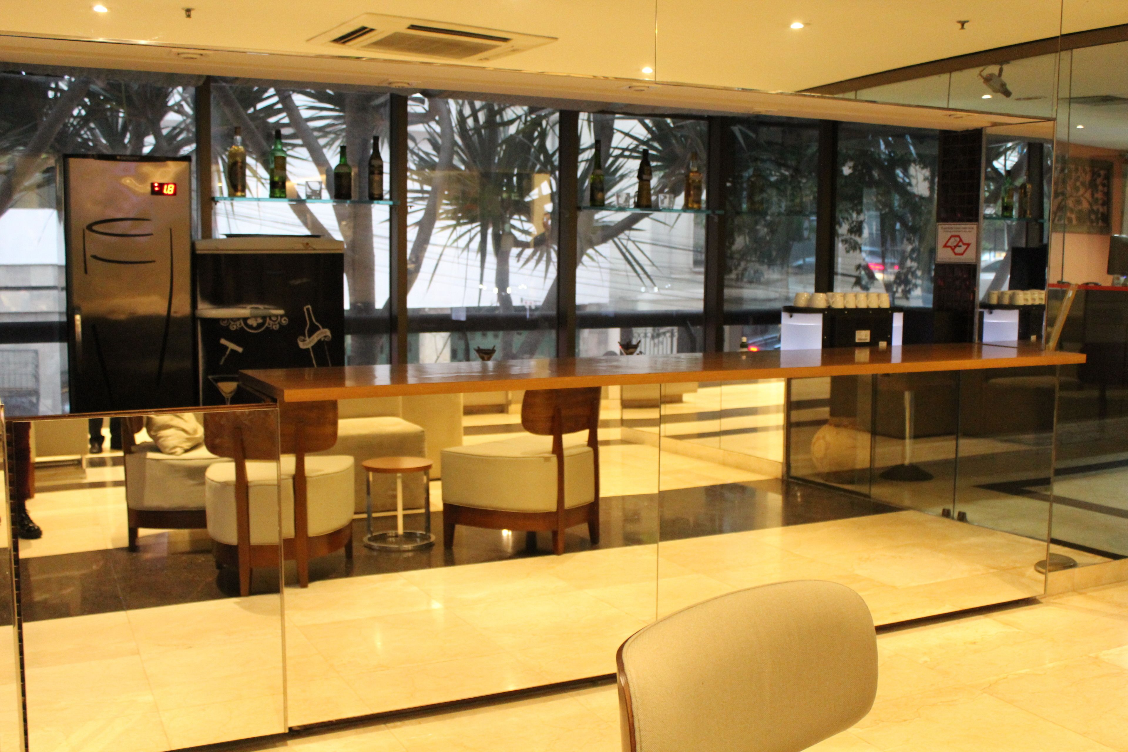 A modern bar area with a glass partition, seating, and a refrigerator.