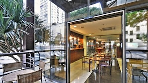 Un café moderno con paredes de vidrio, mobiliario de mimbre y vistas a la ciudad.