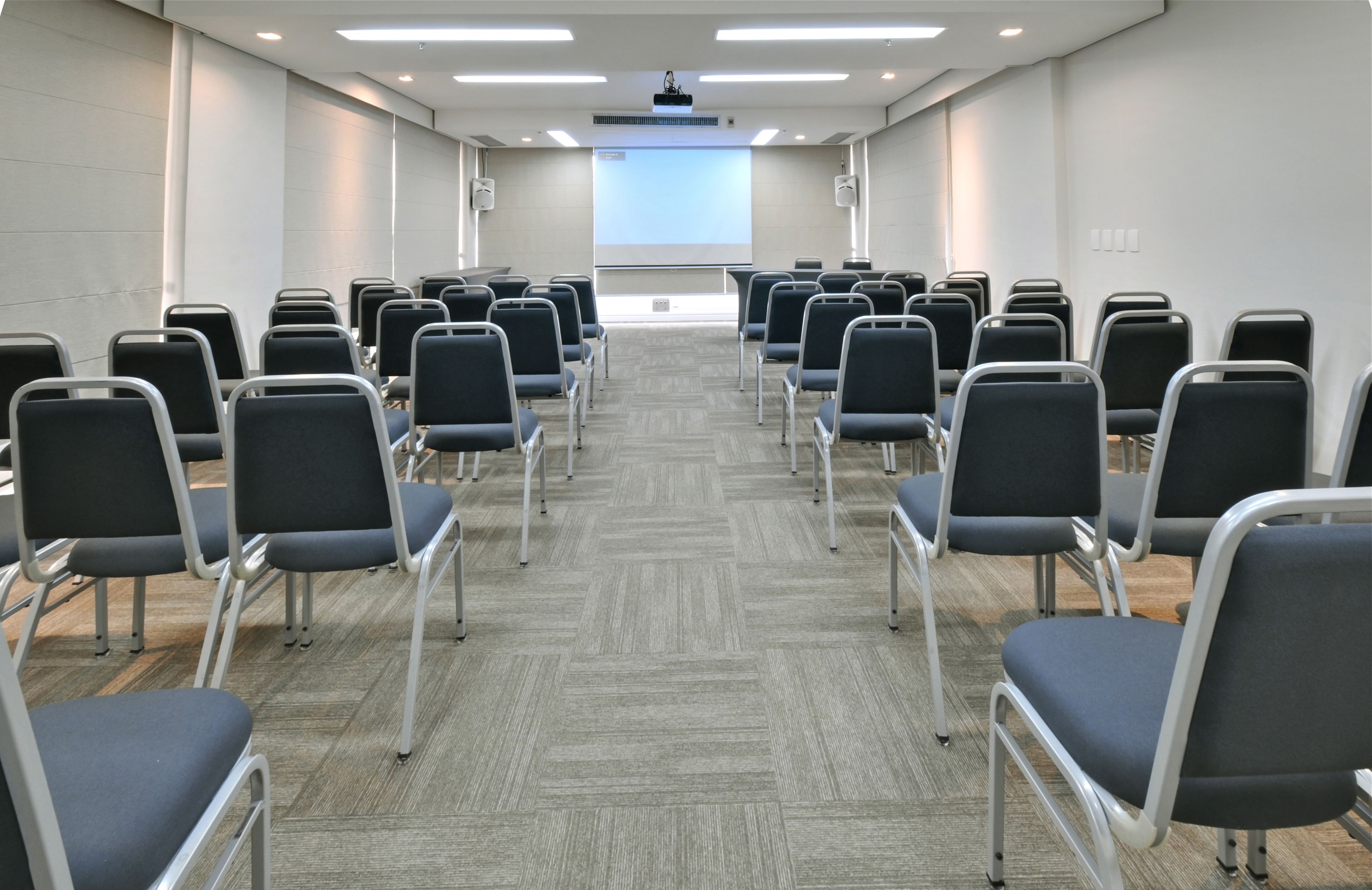 A conference room with rows of chairs facing a projector screen.