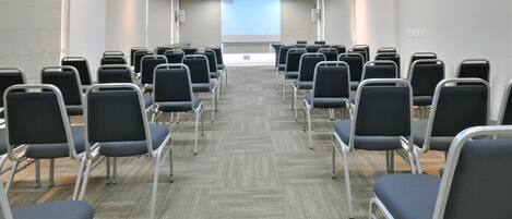 A conference room with rows of chairs facing a projector screen.