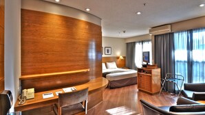 Habitación de hotel con un mostrador de recepción de madera, una cama con cabecera, un escritorio con teléfono, una silla, un televisor y un armario.