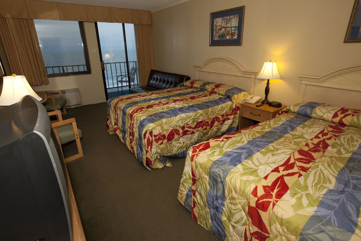 Habitación de hotel con dos camas, un escritorio, una silla, una lámpara y vista al mar.