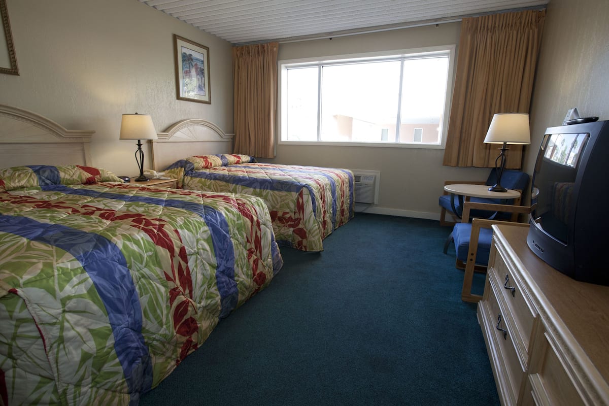 Habitación de hotel con dos camas, un escritorio, una silla, un televisor y una ventana con cortinas.