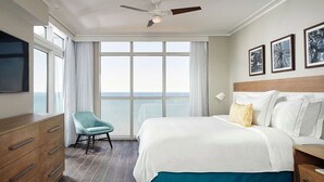 Habitación de hotel con una cama grande, una silla, un aparador, un ventilador de techo y vistas al mar.