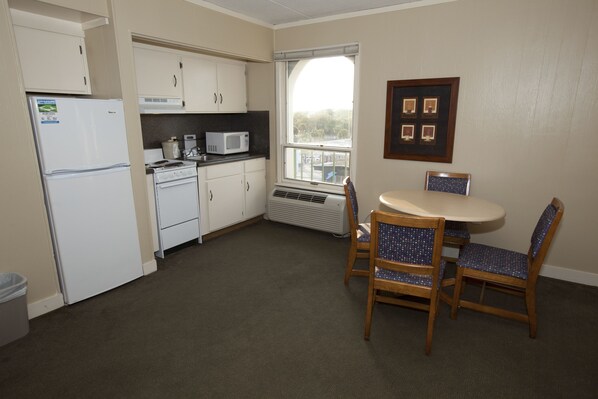 A compact kitchen with a refrigerator, microwave, stove, and a dining table with chairs. - Driftwood at the Boardwalk (Myrtle Beach)