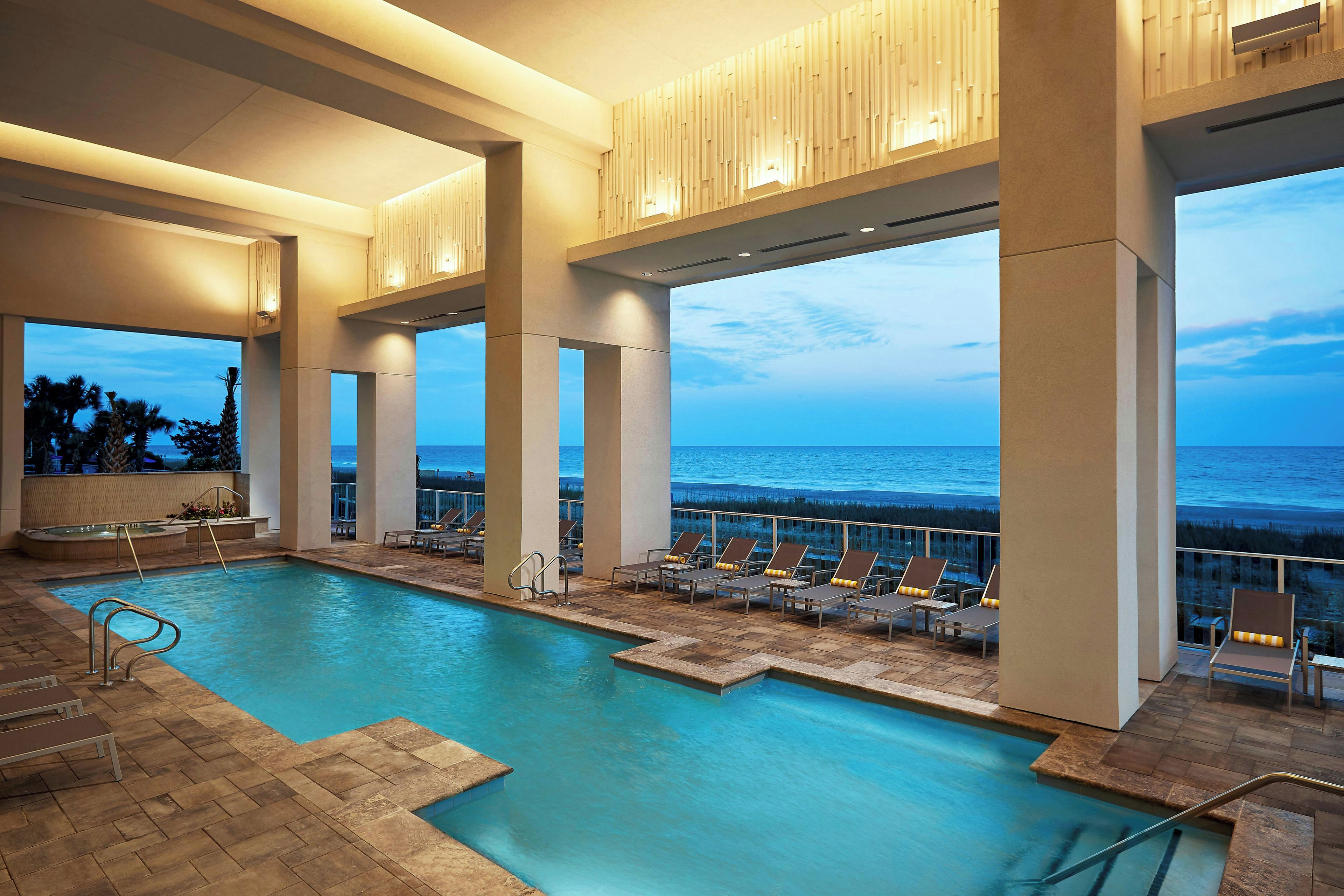 Un espace piscine offrant une vue dégagée sur l’océan, avec des chaises longues et un jacuzzi.