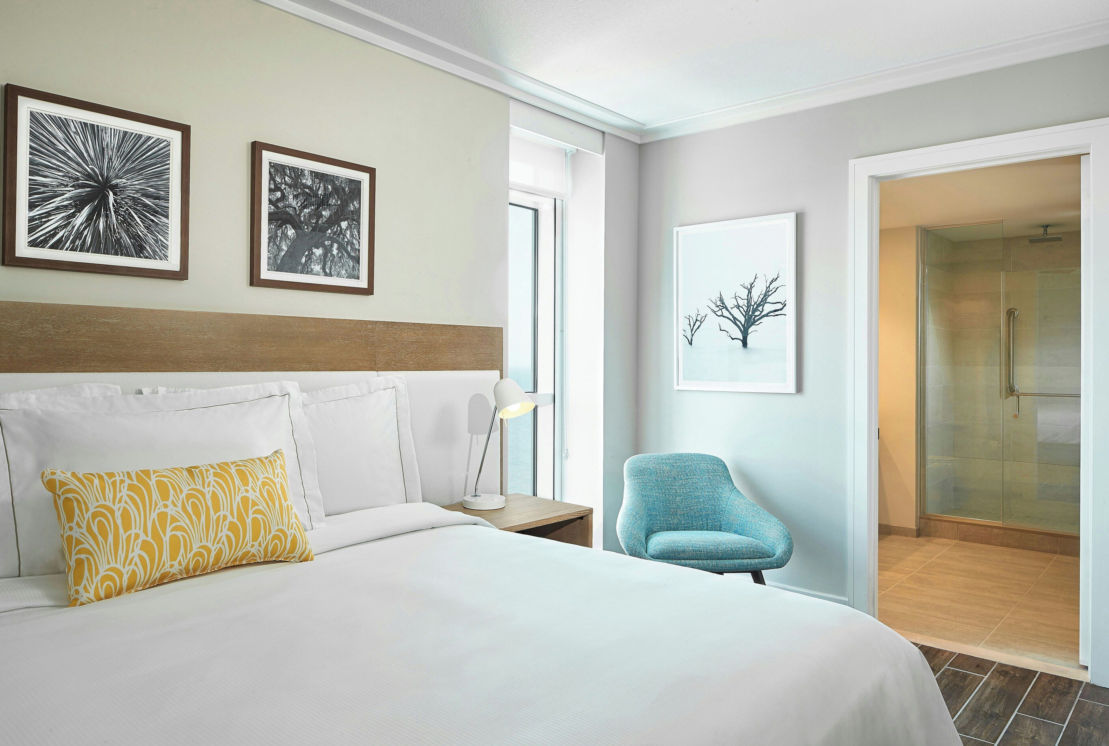 Een hotelkamer met een bed, nachtkastje, lamp, stoel en douche.