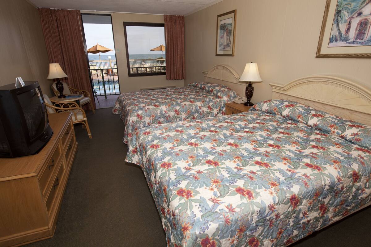 Habitación de hotel con dos camas, televisión, escritorio y balcón con vista a la playa.
