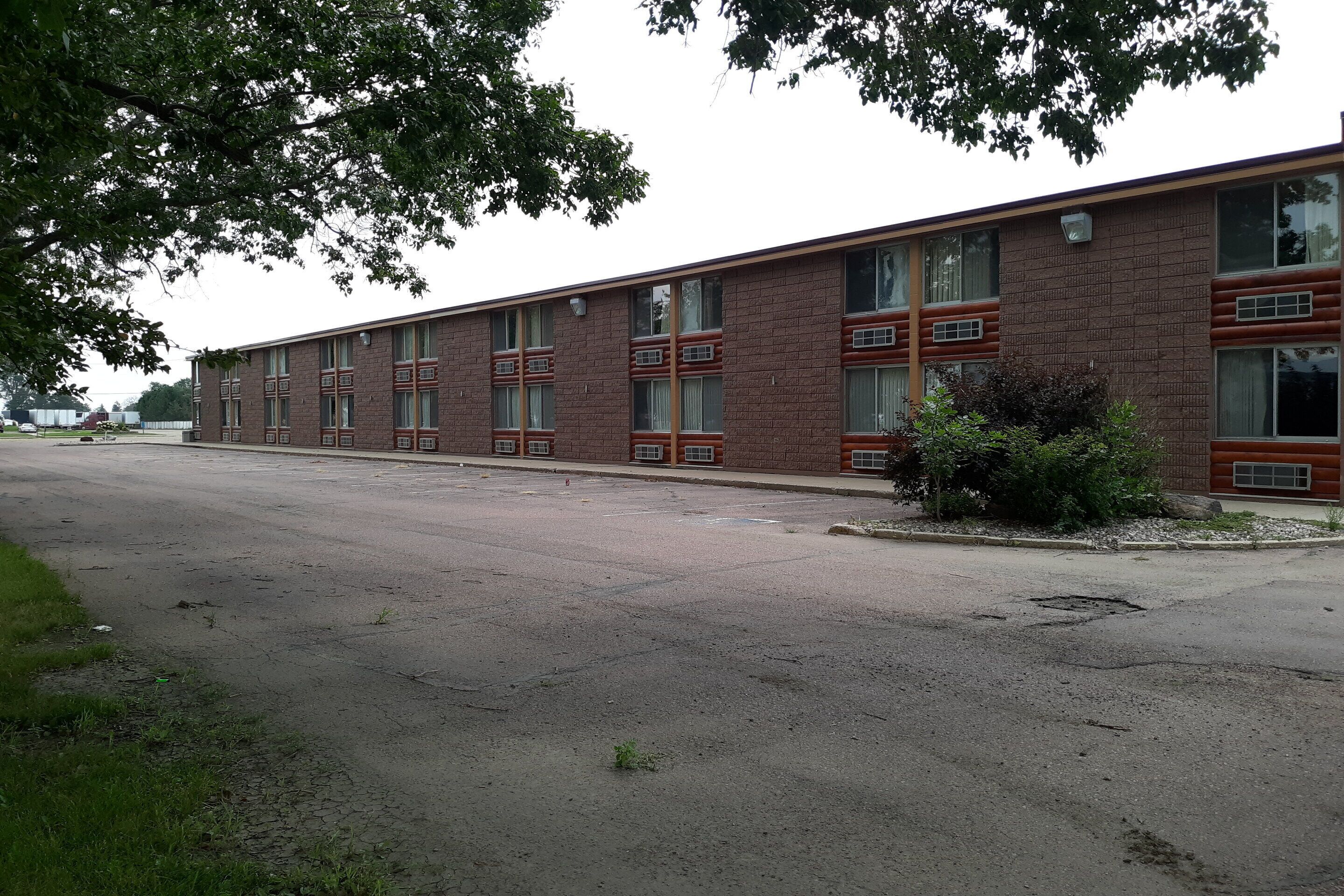 A long, single-story brick building with multiple windows and a parking lot in front.