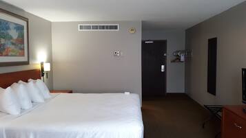 A hotel room with a large bed, a desk, a chair, a TV, and a door.