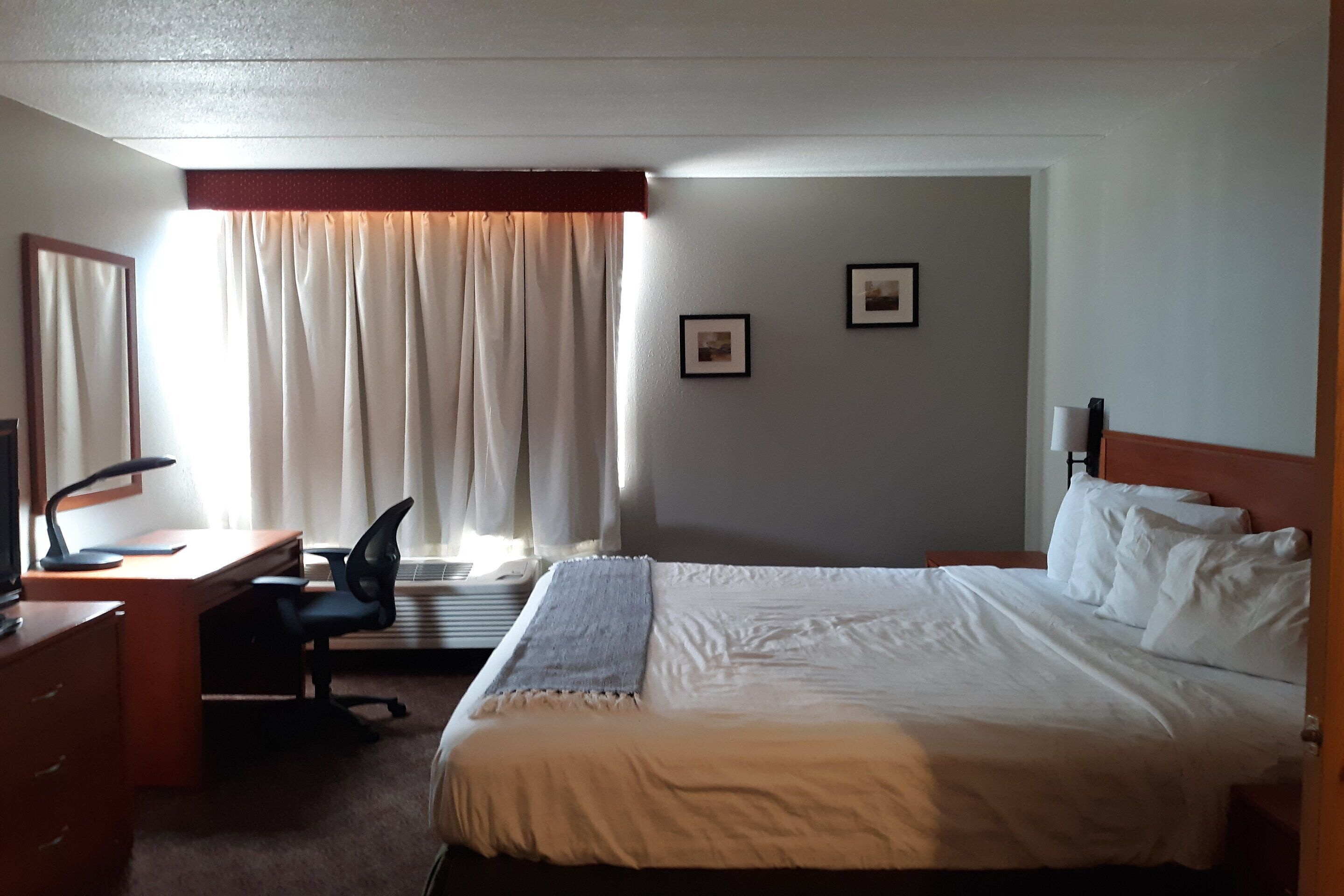 Een hotelkamer met een bed, bureau, stoel en twee foto's in lijsten aan de muur.