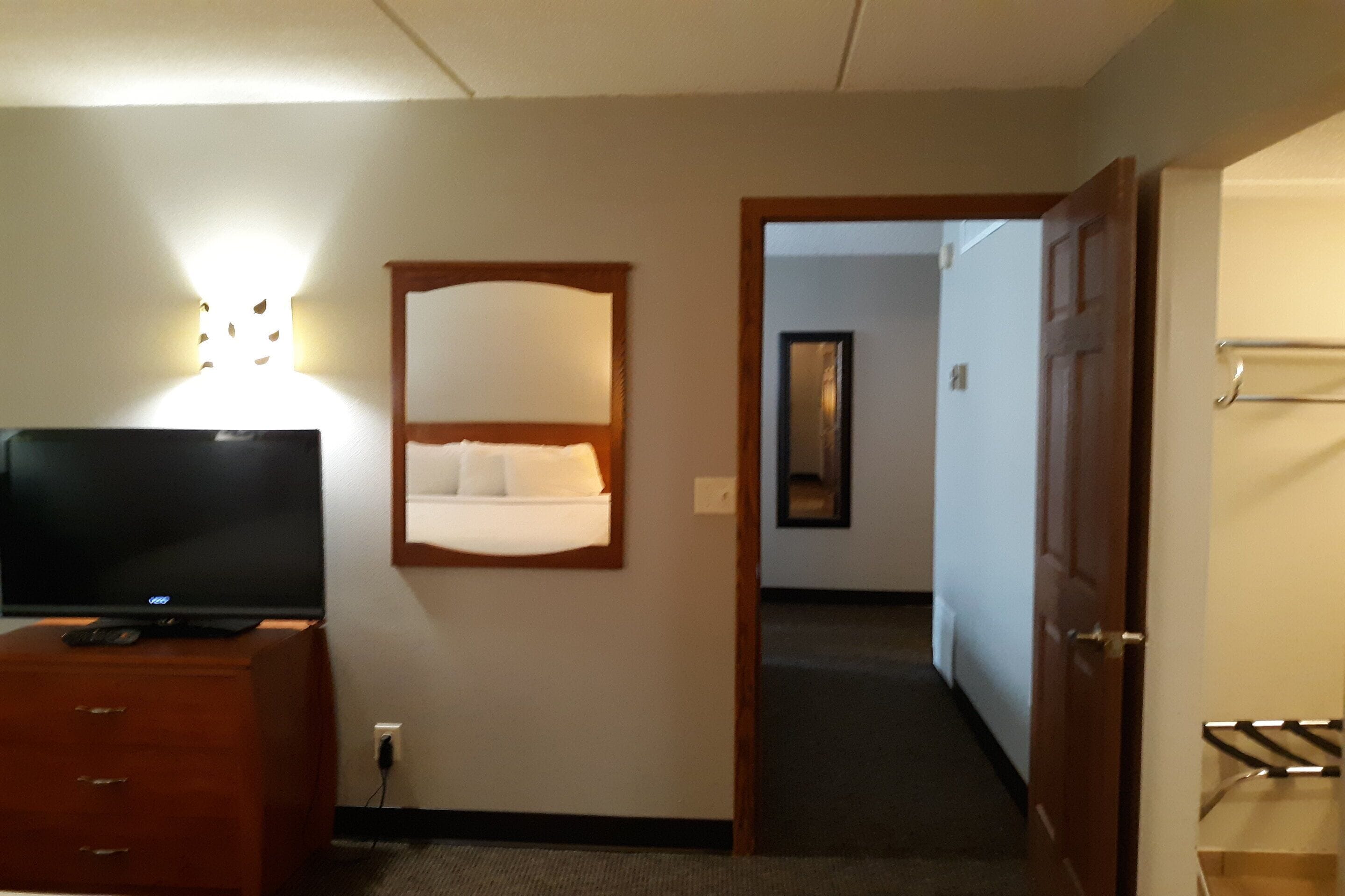 Habitación de hotel con una televisión de pantalla plana sobre un aparador de madera, una mesita de noche con lámpara y un espejo en la pared.