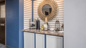 A hotel reception area with a blue wall, a large mirror, and a counter with coffee-making equipment. - The Dakota (Sioux Falls)