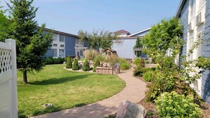 A residential area with a paved walkway, a stone bench, and a variety of shrubs and trees. - The Dakota (Sioux Falls)