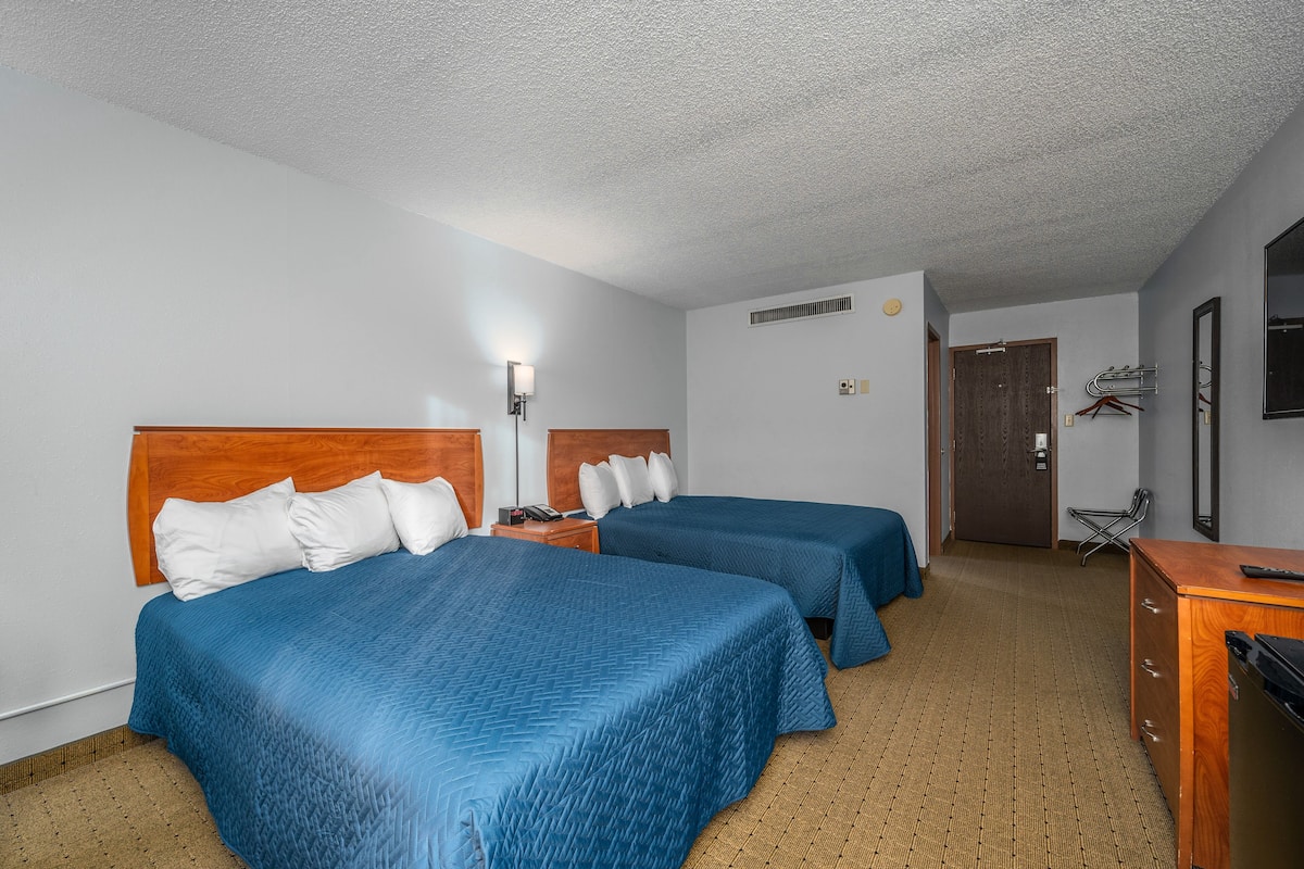 Ein Hotelzimmer mit zwei Betten, einem Schreibtisch, einem Stuhl und einem Kleiderschrank.
