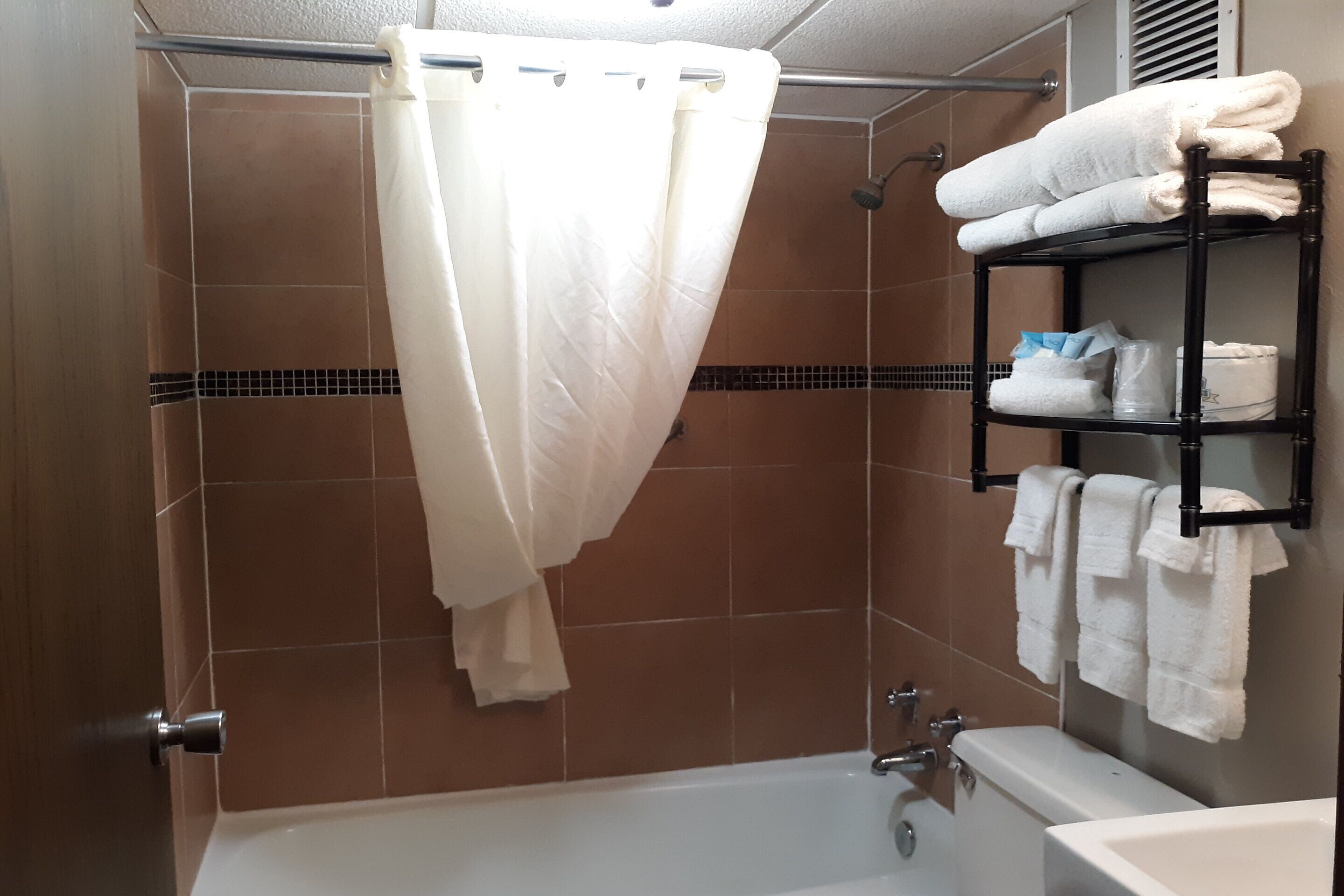 Un espace douche avec un rideau blanc, une étagère avec des serviettes et une baignoire.