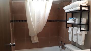 Un espace douche avec un rideau blanc, une étagère avec des serviettes et une baignoire.