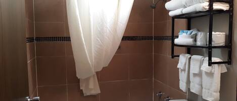 Un espace douche avec un rideau blanc, une étagère avec des serviettes et une baignoire.