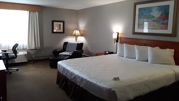 A hotel room with a large bed, a desk with a chair, a lamp, and a painting on the wall. - The Dakota (Sioux Falls)