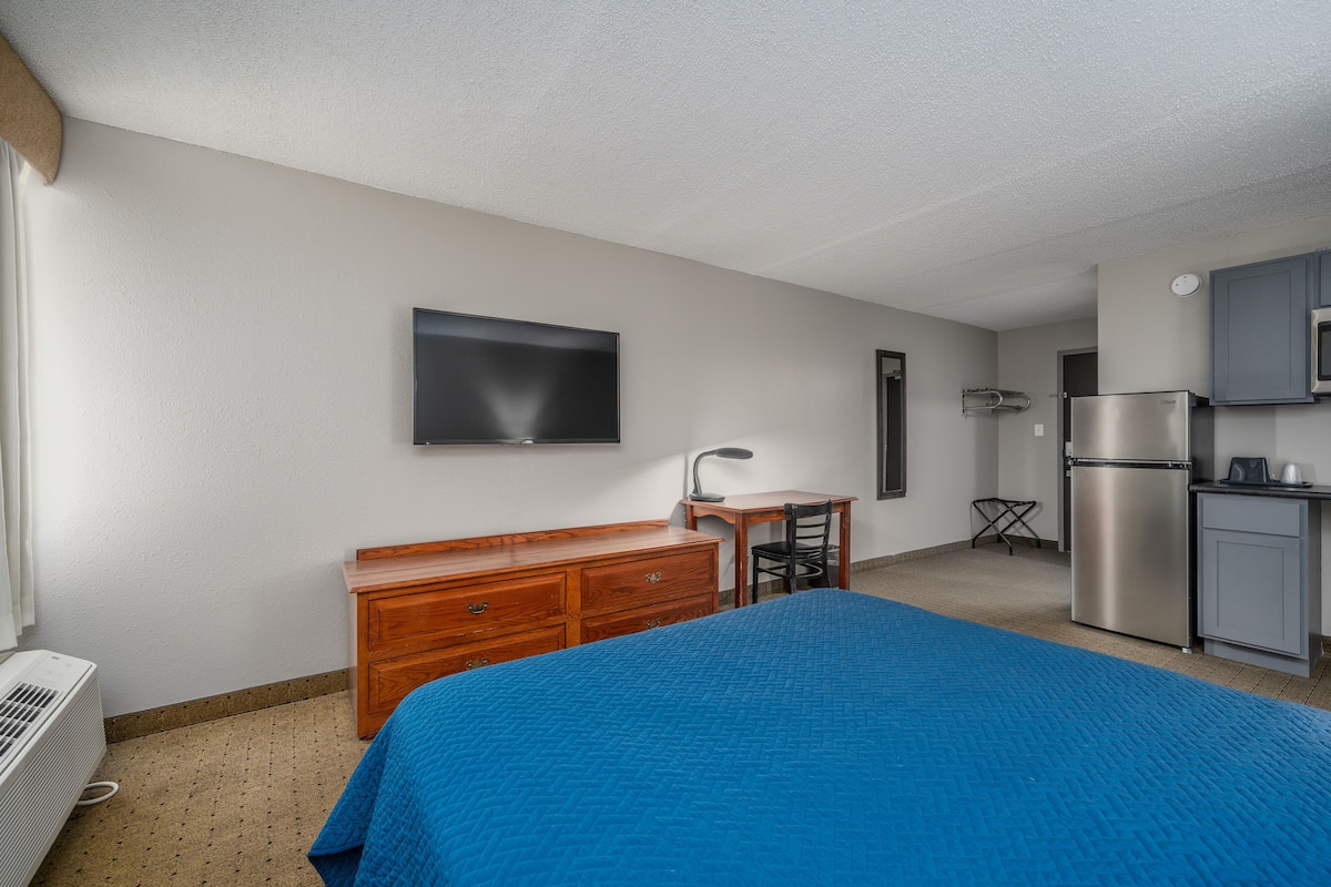 Ein Hotelzimmer mit Bett, Schreibtisch, Stuhl, Fernseher, Kühlschrank und Mikrowelle.