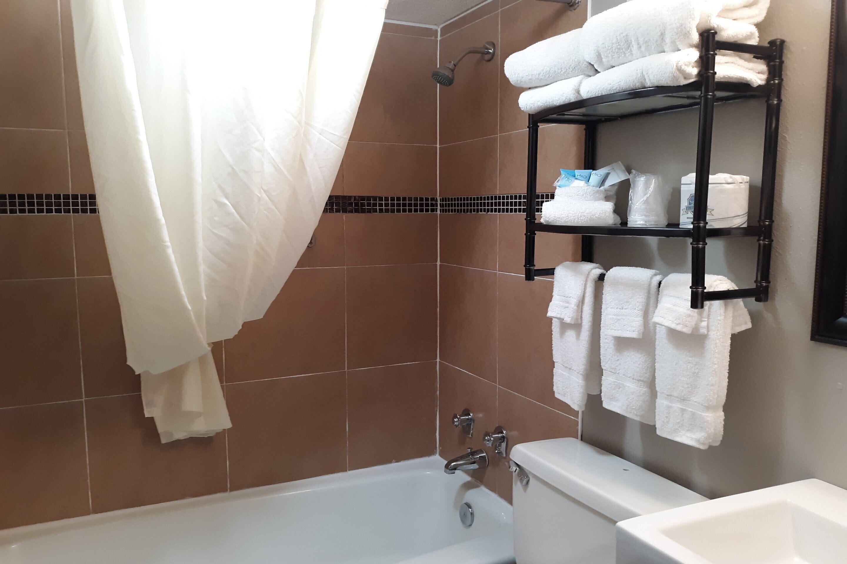 A bathroom with a bathtub, a shower, and a toilet. There are white towels on a shelf and a shower curtain.