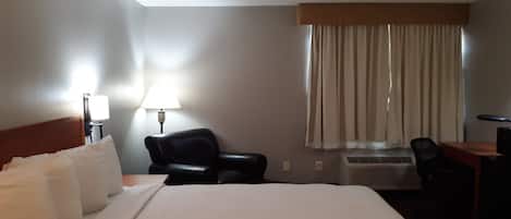 Une chambre d’hôtel avec un grand lit, un bureau, une chaise, une lampe et une fenêtre avec des rideaux.