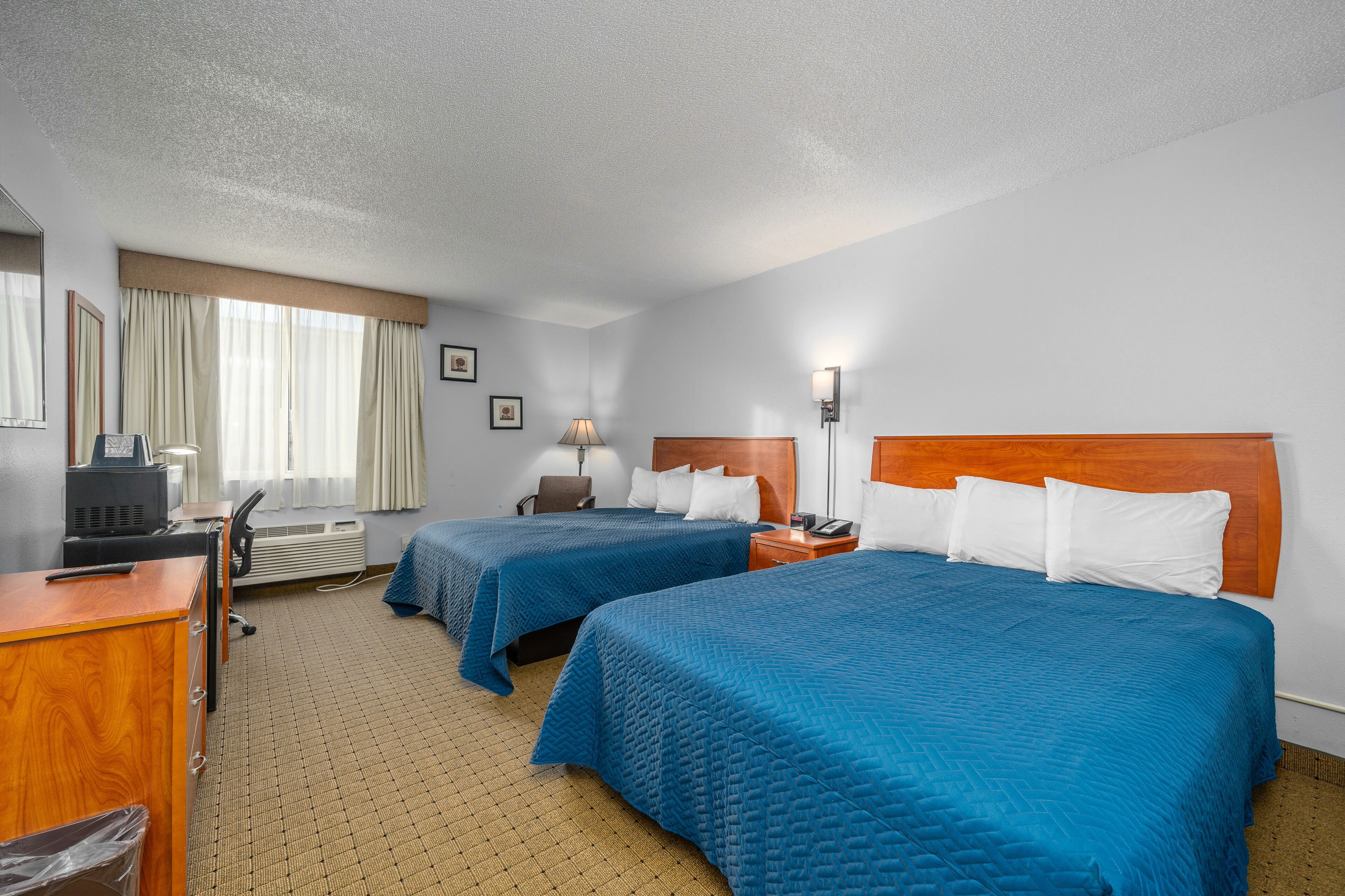 A hotel room with two beds, a desk, a chair, a lamp, and a television.