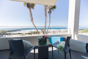 Un balcón con vistas a la playa, dos sillas, una mesita y una cesta con objetos.