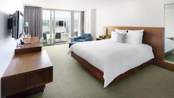 Habitación de hotel con una cama grande, escritorio, silla, televisor y balcón con vistas.