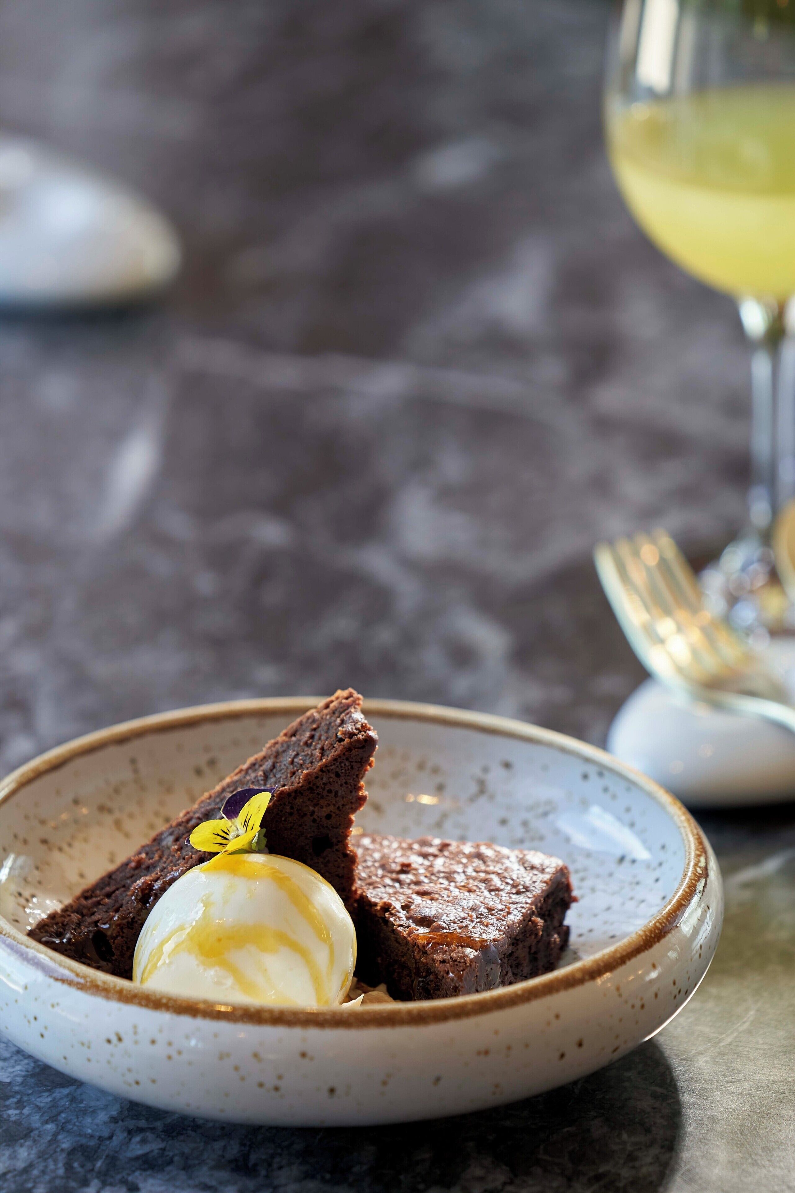 A dessert plate with a chocolate cake and a scoop of ice cream, accompanied by a glass of white wine.