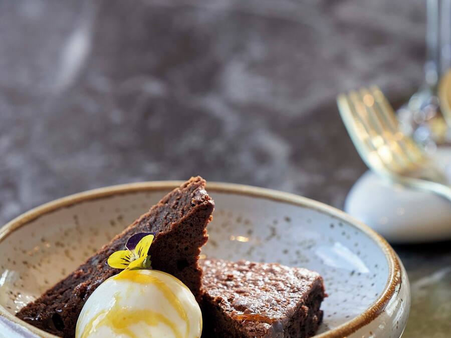 A dessert plate with a chocolate cake and a scoop of ice cream, accompanied by a glass of white wine.