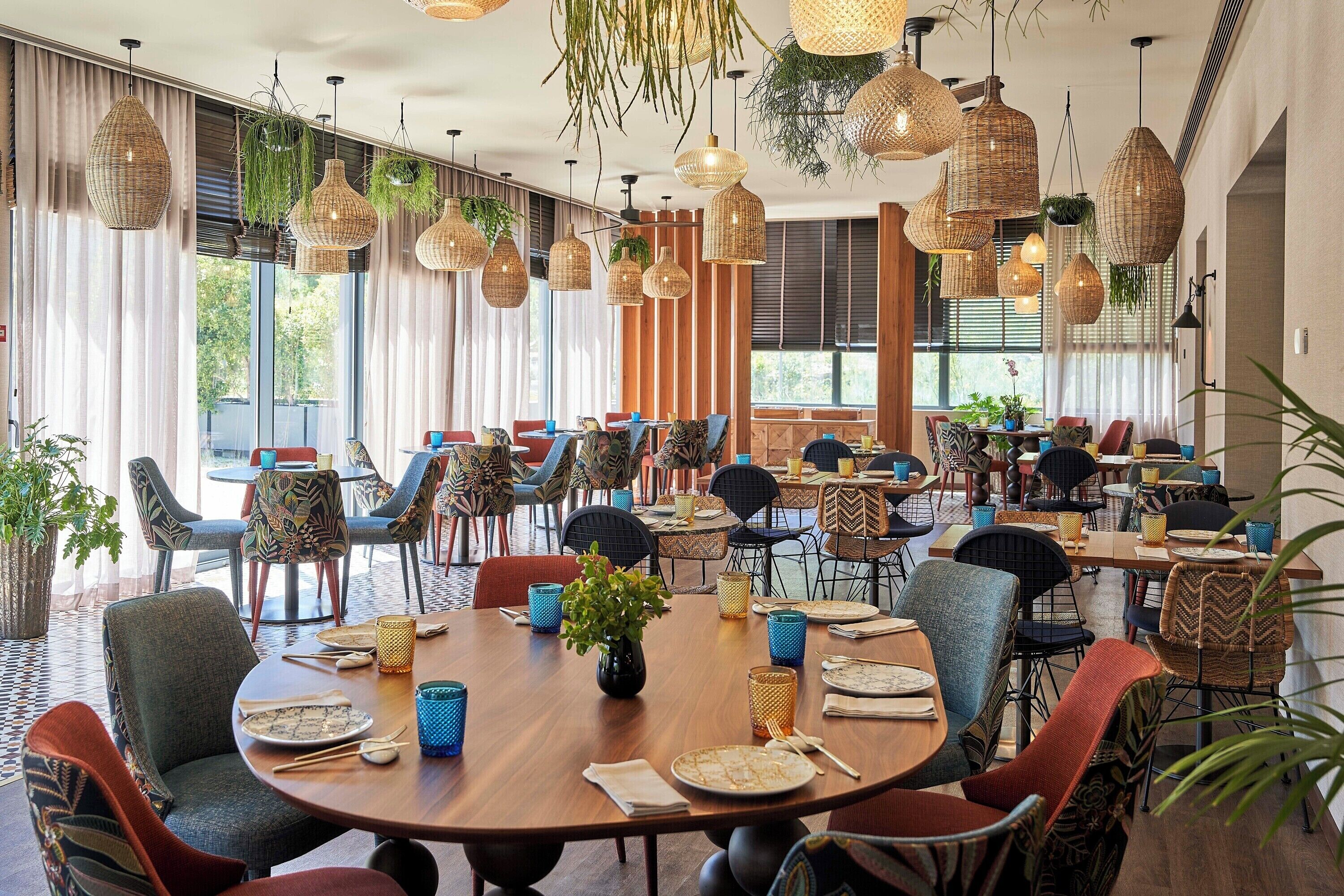Un comedor espacioso con mesas redondas, lámparas colgantes de mimbre y diversas sillas.
