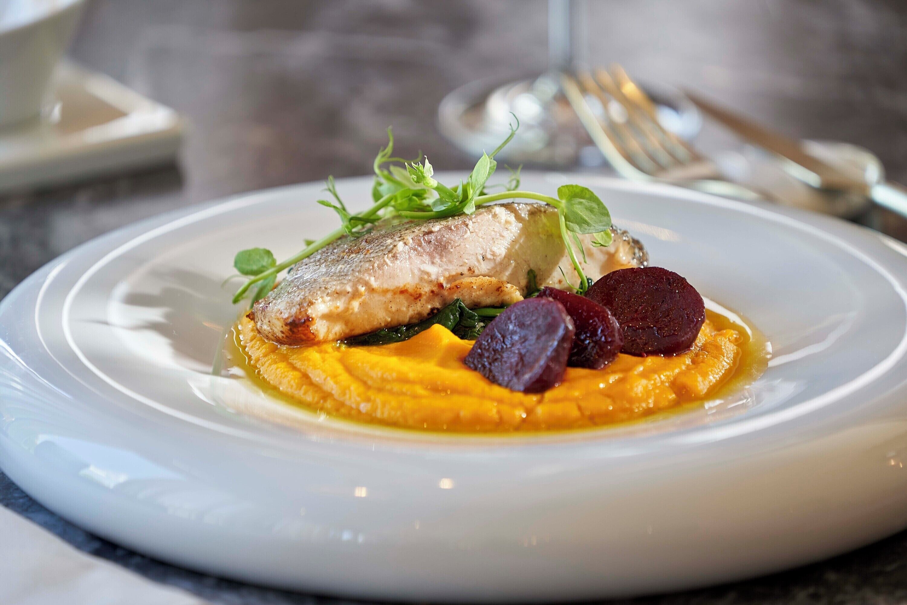 A plate of food with a fish, vegetables, and a sauce.