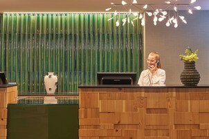 Un mostrador de recepción con detalles de paneles de madera, un jarrón con flores y un panel vertical verde al fondo.