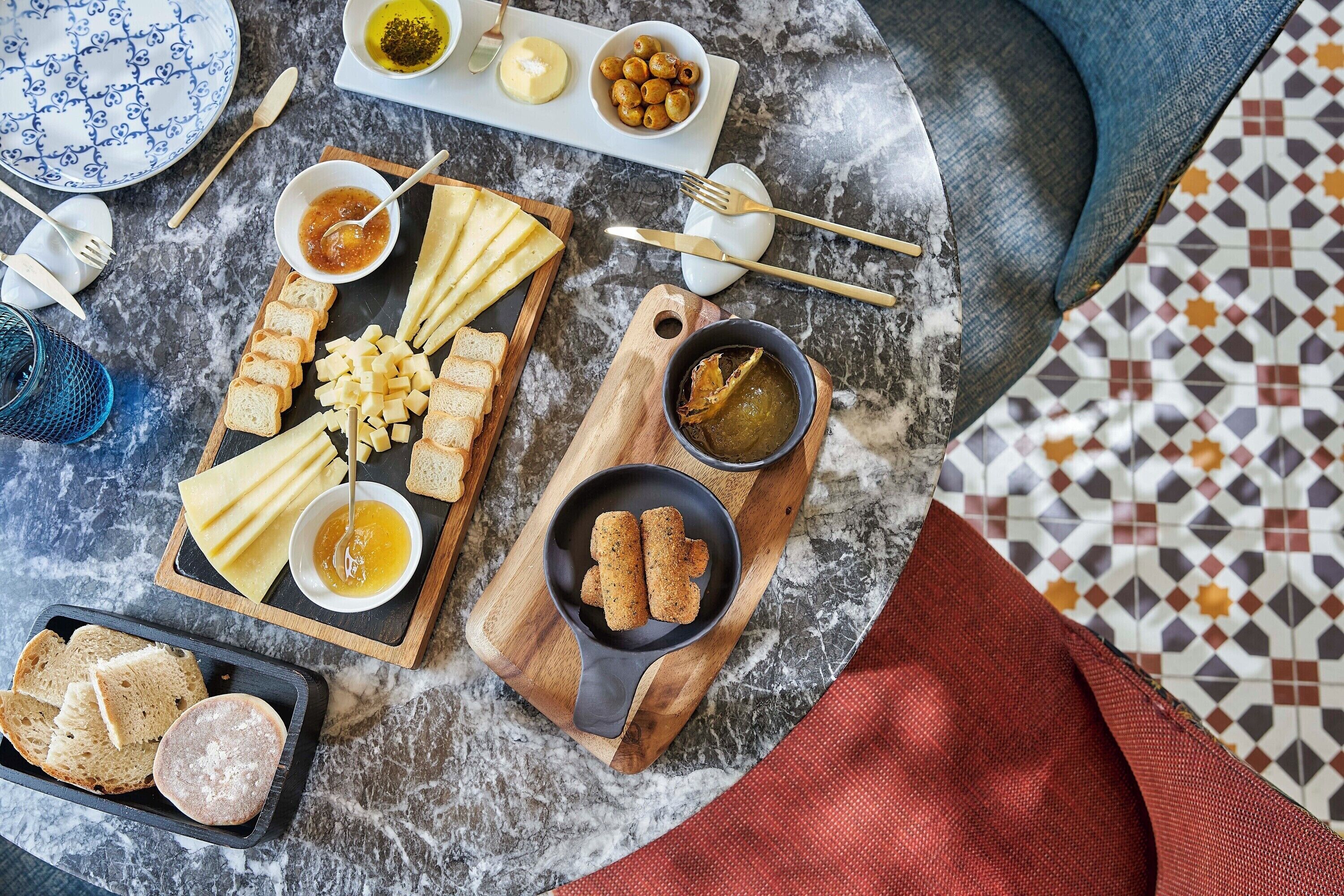Ein Tisch mit verschiedenen Käsesorten, Oliven und Brot, zusammen mit Beilagen und Besteck.