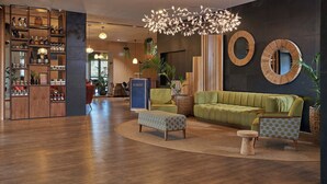 Un interior moderno con un sofá verde, un otomano estampado, sillones, una estantería de madera y un espejo circular único.