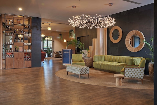 Un interior moderno con un sofá verde, un otomano estampado, sillones, una estantería de madera y un espejo circular único.