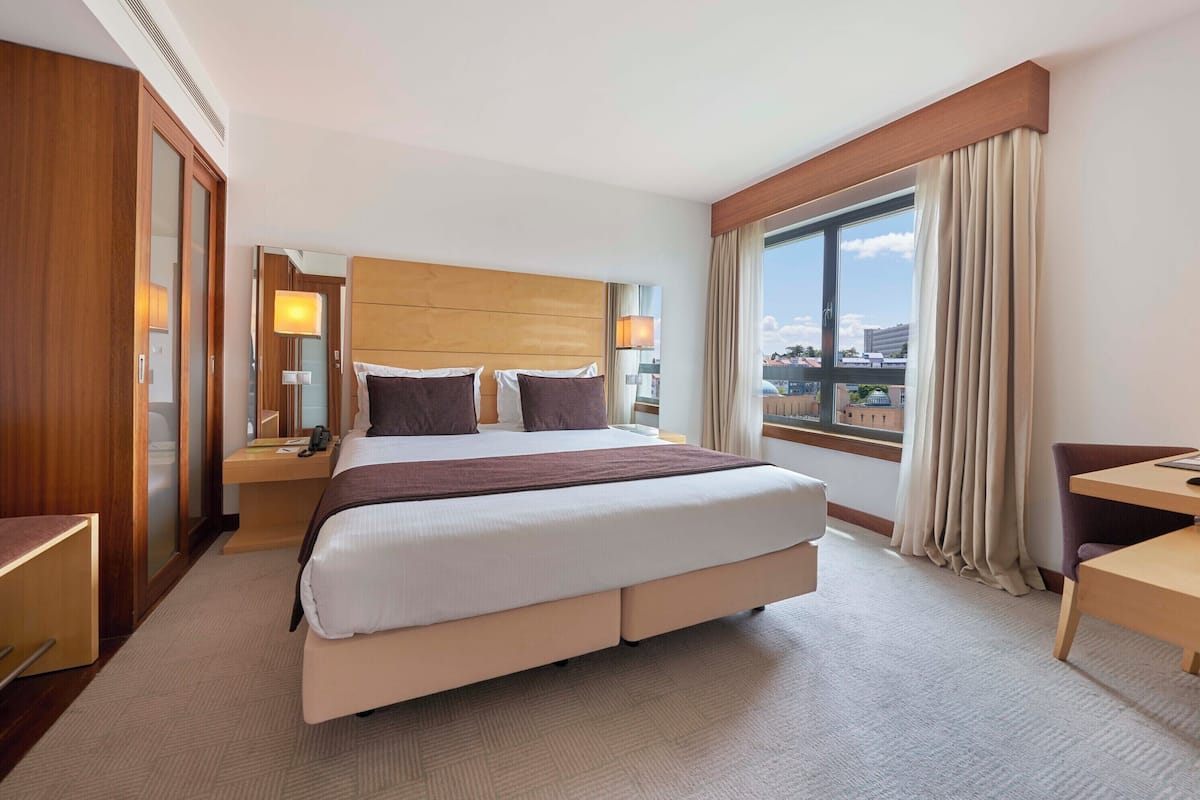 Ein Hotelzimmer mit einem großen Bett, Nachttischen, einem Schreibtisch und einem Fenster mit Vorhängen.