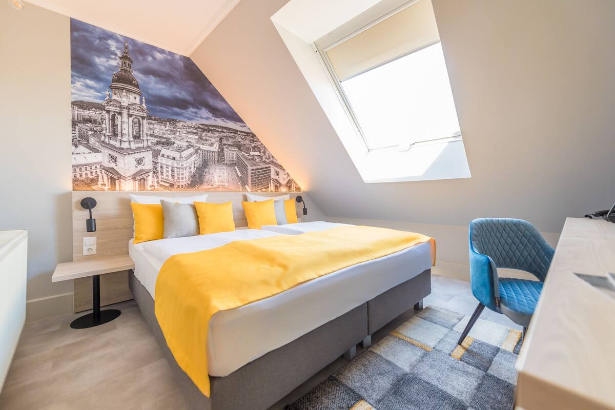 A bedroom with a bed, a desk, a chair, and a cityscape mural on the wall.