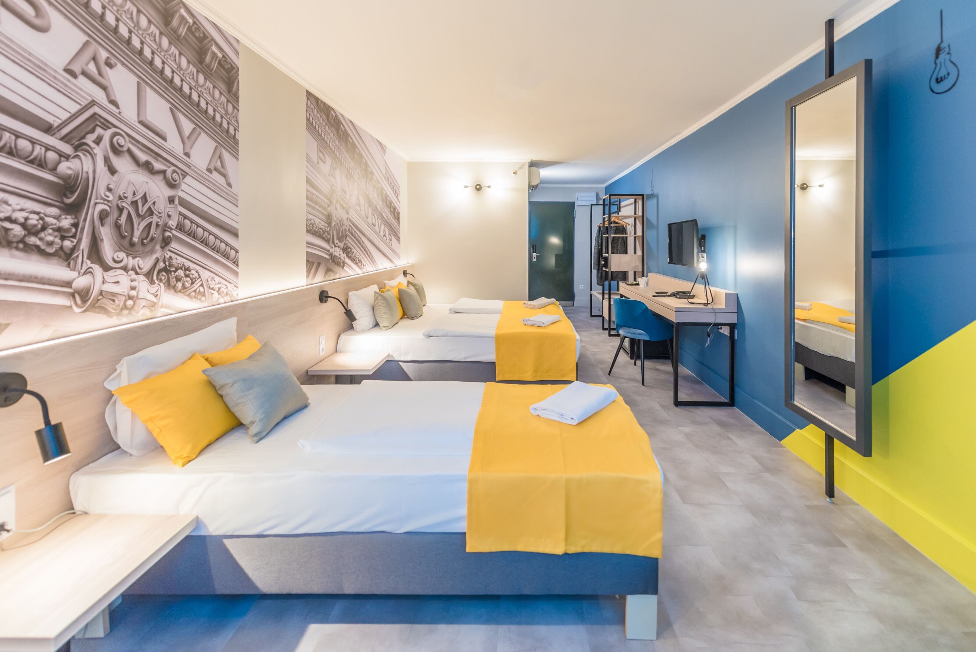 A modern hotel room with two beds, a desk, a chair, and a large mirror.